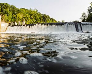 Water from the Columbia Lake spills over a dam. A tall masonry structure is on the shore.