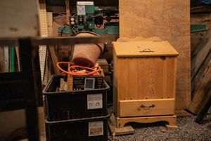 A wooden cabinet sitting on the floor of a wood shop with boxes beside it. 