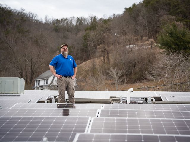 A person stands outside among several solar panels.