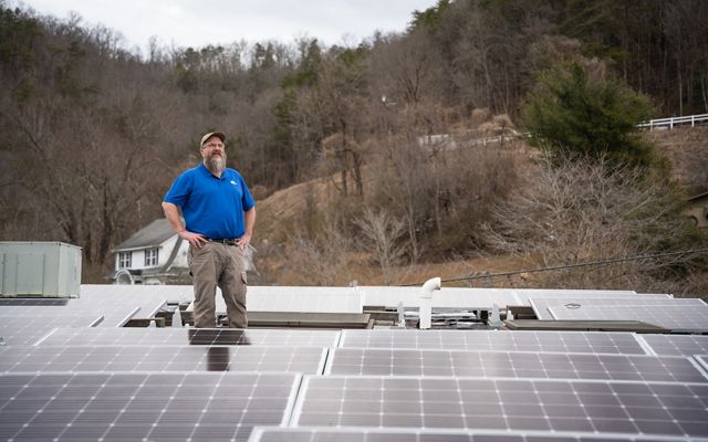 Man standing on a roof surrounded by a solar power installation.