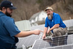 Two people look over solar installation on a roof. 