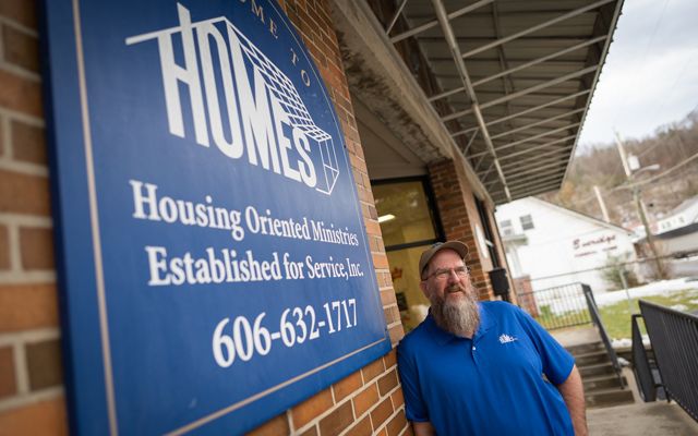 Man in a blue shirt posing next to a sign that reads HOMES, Inc.
