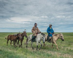 Herders ride on horses on the grassland steppe of Eatern Mongolia's Tosonhulstai Nature Reserve.