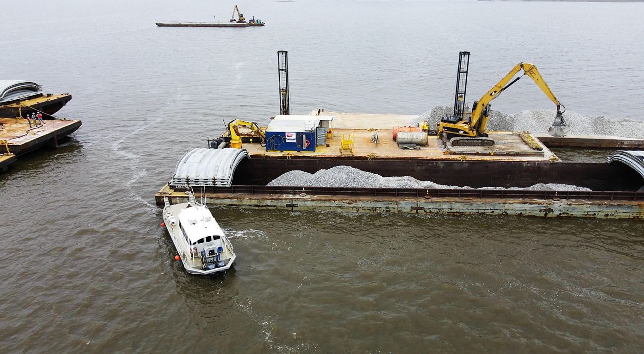 A barge floats in calm waters next to a pile of gray shells.