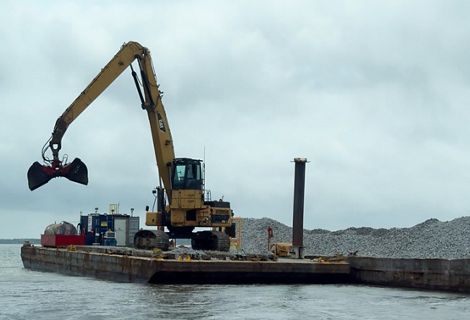A large yellow piece of equipment lowers something into the water.