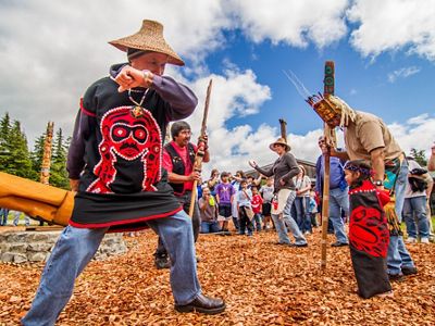 Several colorfully dressed adults and one child dance in a group while other people watch them.