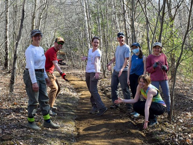 A group of men and women pose around a trail they've been maintaining.
