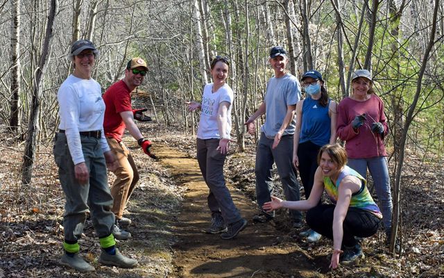 A group of men and women pose around a trail they've been maintaining.
