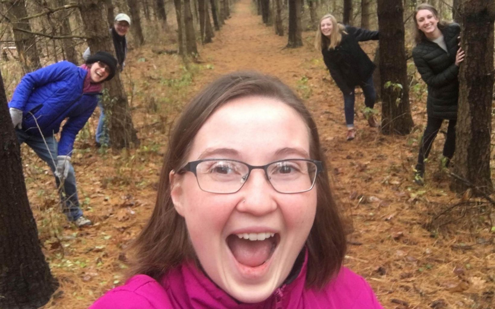 Group of women hiding behind trees on a nature trail. 