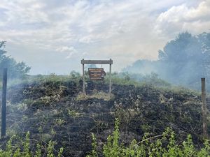 A sign for Broken Kettle Grasslands Preserve sits in the middle of a black patch of land that was just burned..