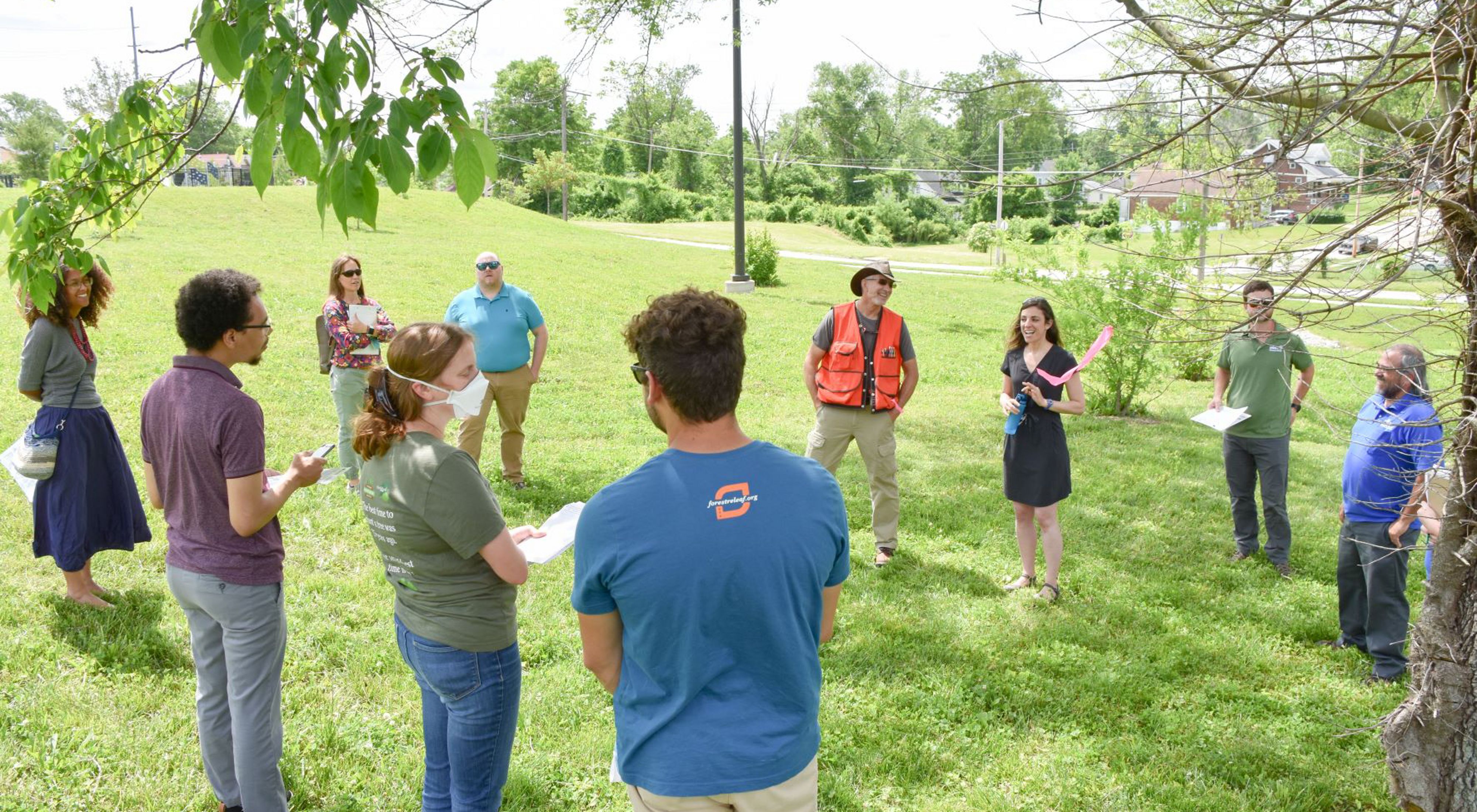 A small group of individuals gather in an outdoor lot to listen to a speaker.