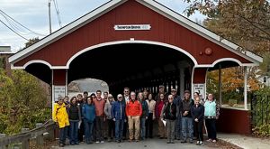 A group of people posing in front of a red wooden covered bridge.