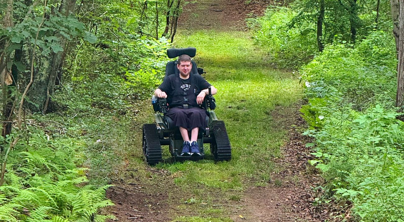 A person explores surrounding woods in a wheelchair made for outdoor use.