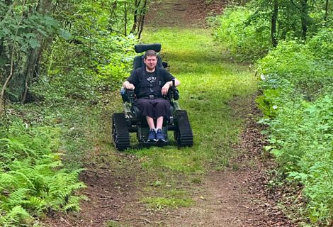 A person uses a mobile, all-terrain wheelchair to move through a forest.