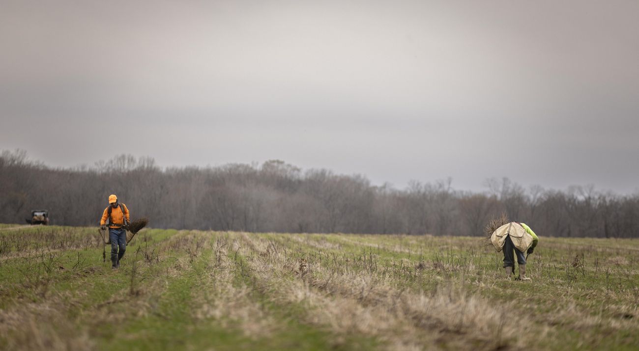 two workers with shovels and gear in a field.