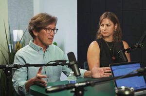 Two people sit at a table near a microphone.