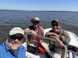 Three men wearing hats, pose on a small boat for a picture.