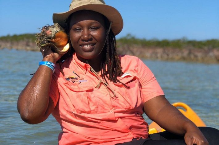 a black woman with a hat holding a queen conch outside