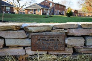 A plaque set into a stone wall enclosing a green community area.