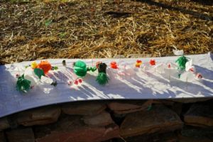 Small art projects are displayed on a long piece of white fabric laid out on the ground.