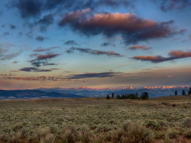 Photo of sun setting over the Tunk Creek Valley in Washington, shrubs in foreground, setting sun illuminating clouds overhead.
