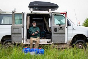 A man sits inside the open side doors of an Econoline van.