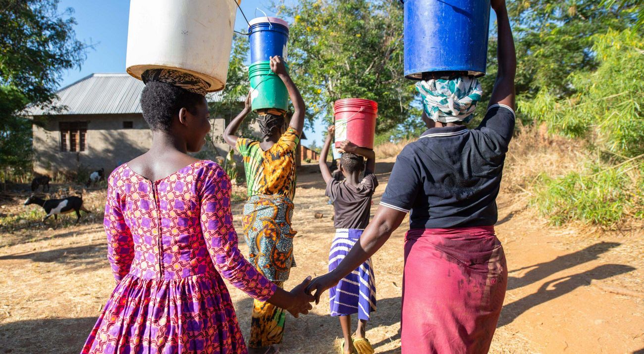 A group of women with buckets on their heads walking away.