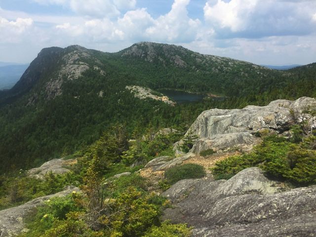 A rocky peak with shrubby green vegetation and a pond close to the summit.