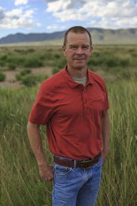 A man stands in a field of tall green grass.