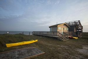 A house sits on a beach; a yellow kayak lies next to the house.