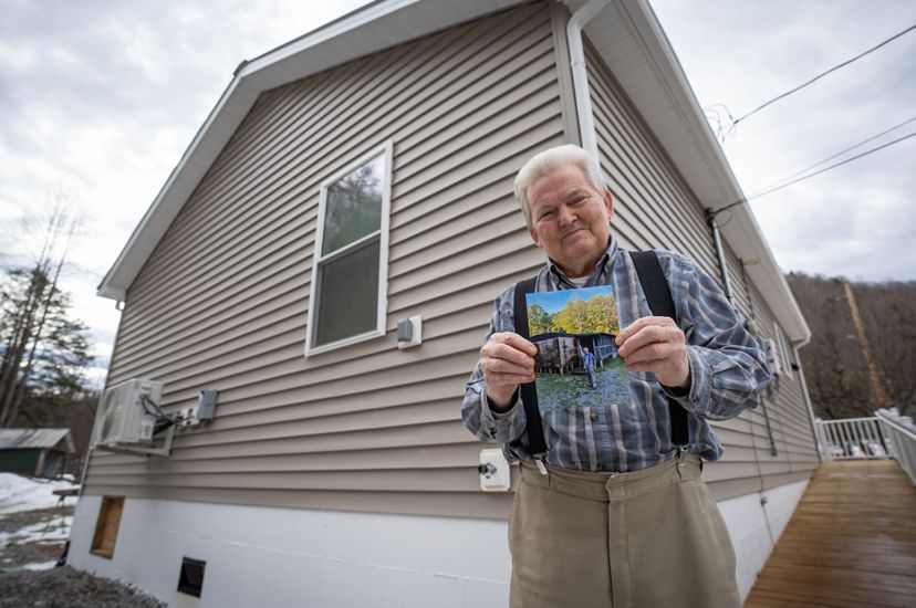 A man smiling and holding a photo of his old home in front of his new, energy efficient house. 