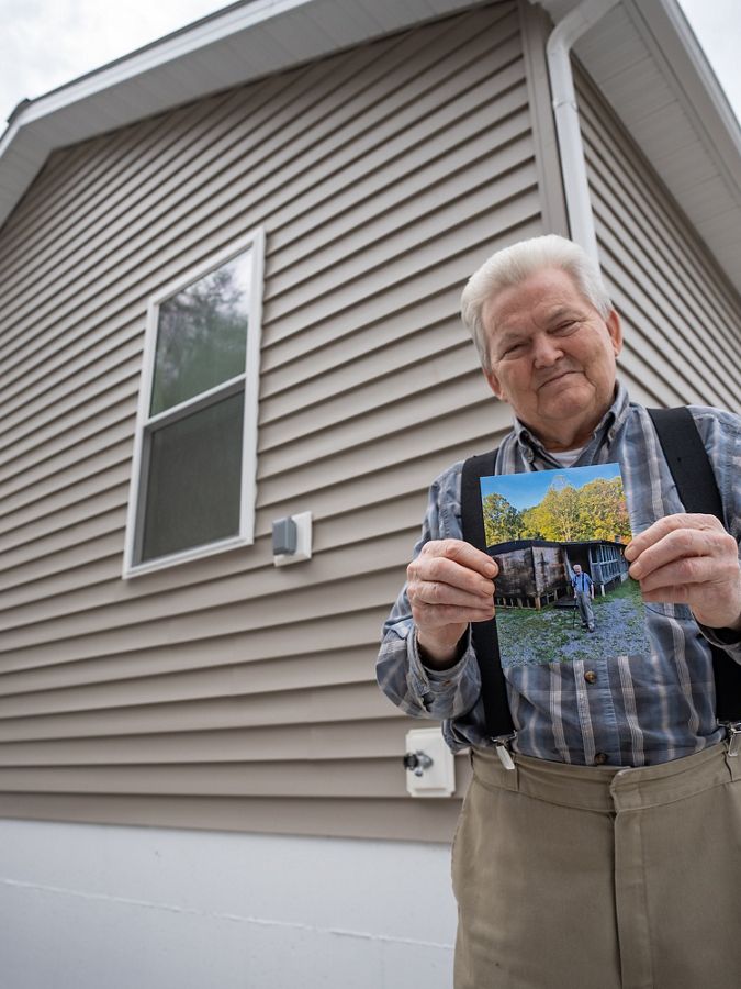 Man smiling and holding a picture in front of a house. 