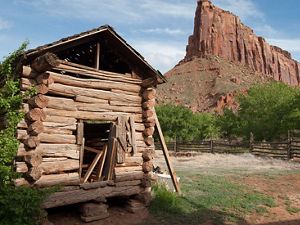 A crumbling wooden barn sits in the foreground with red cliffs looming in the background.