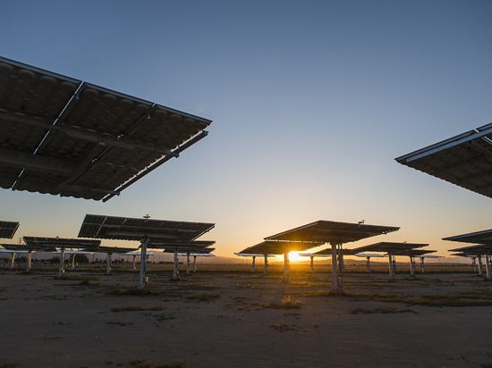 Photo of solar panels in the desert, as sun sets in background.