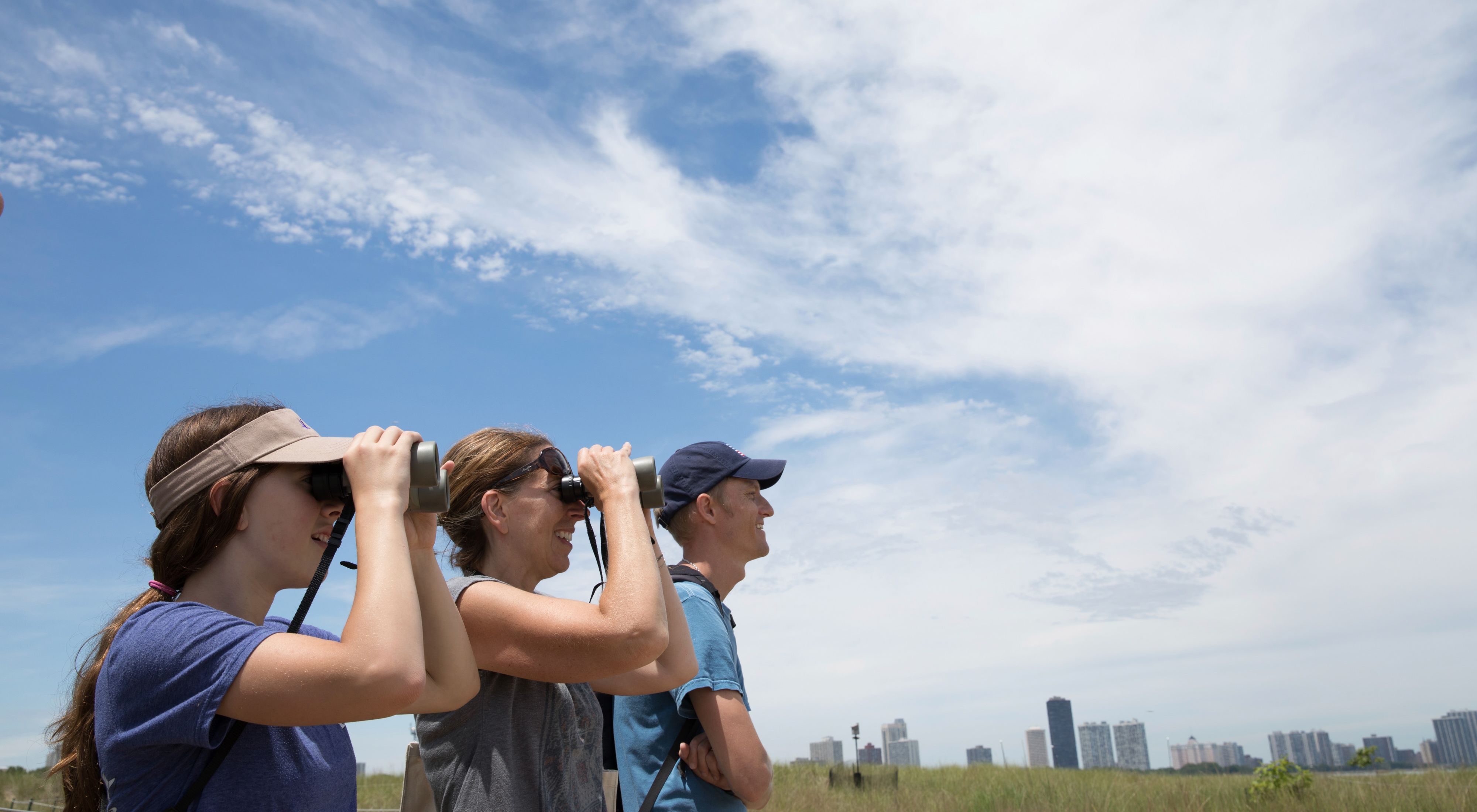 Three people, two with binoculars, look off in the distance in Chicago.