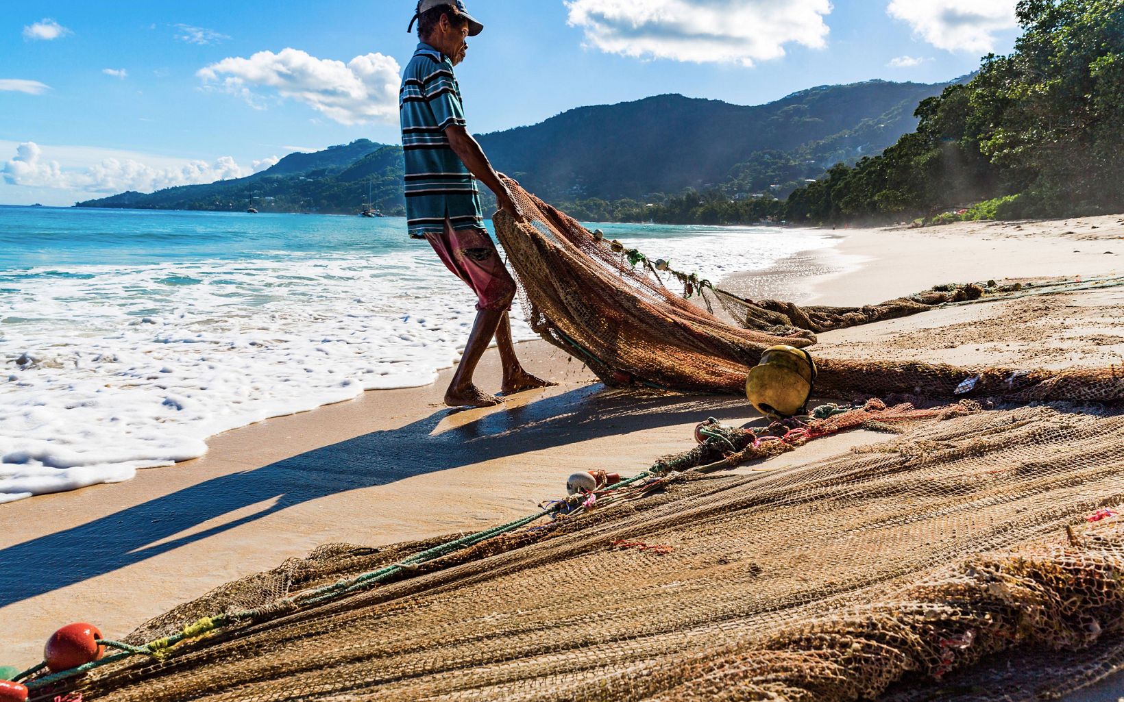 Man pulling a fishing net up the beach.