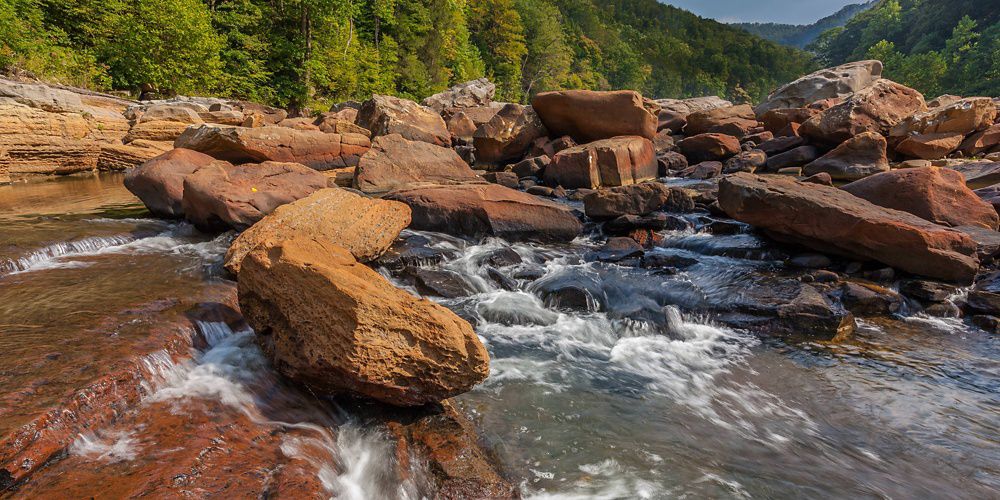 Water tumbling over huge boulders in forested mountainous terrain.