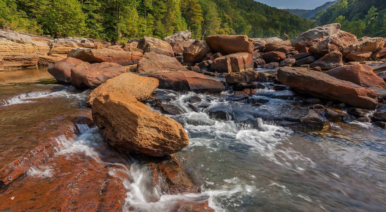 Closeup view of many red boulders with a river trickling through and over them.