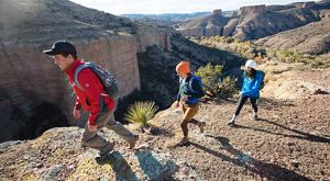 three hikers walking in a line above canyon