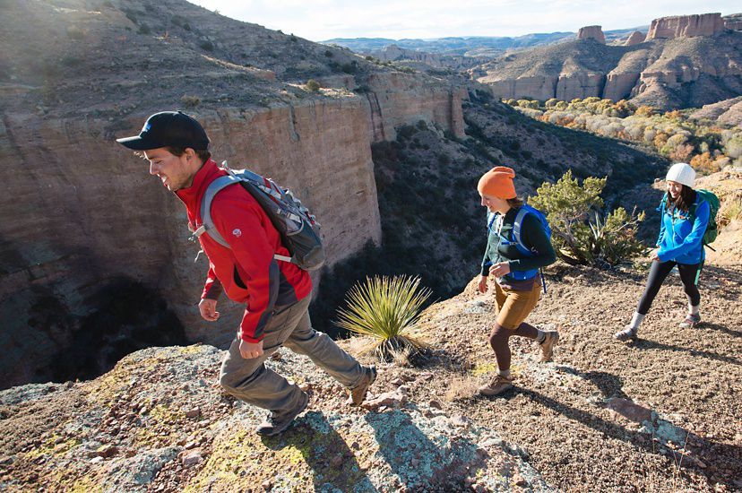 Three people hike along the edge of a desert canyon