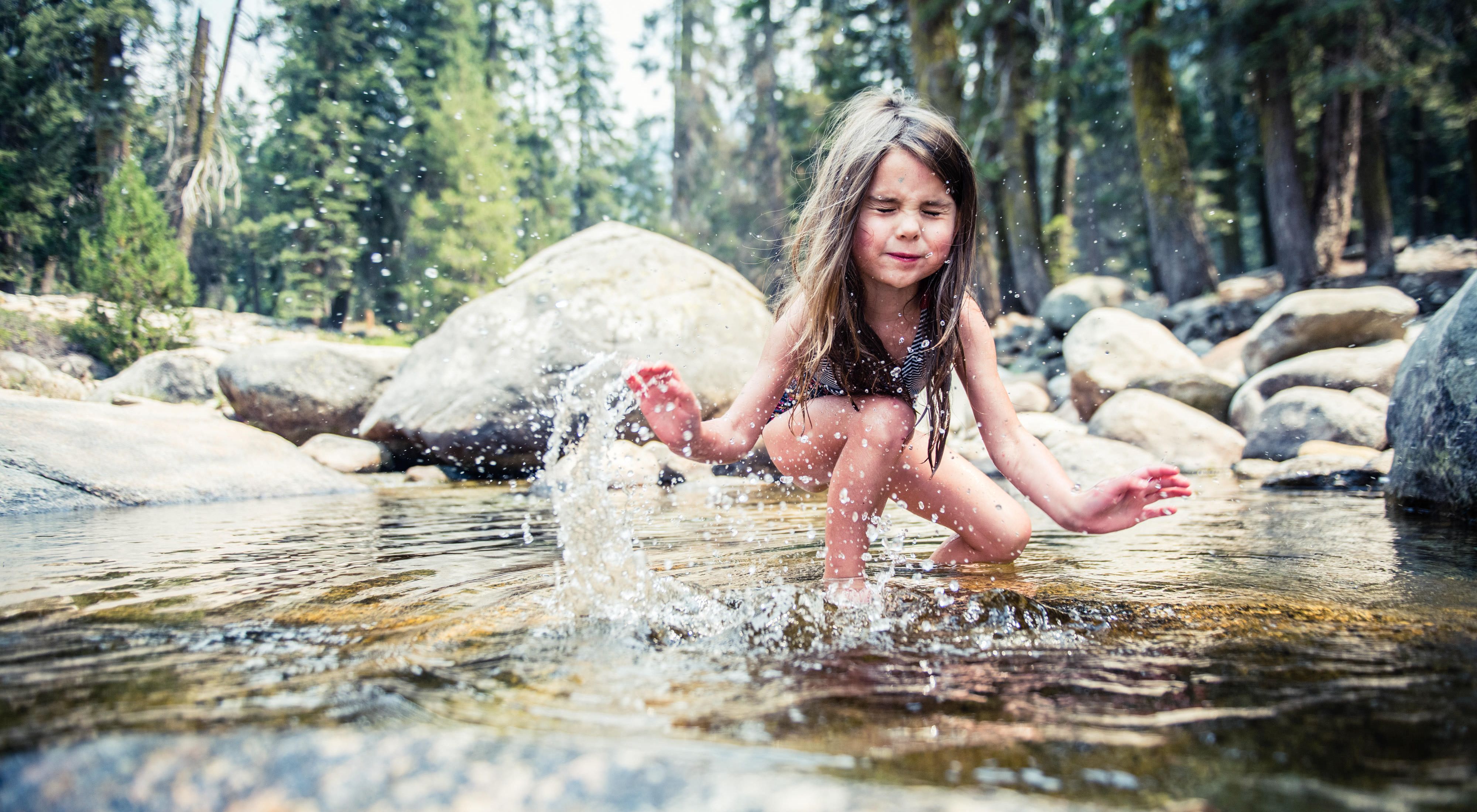 A girl splashes water in front of rocks.