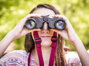 Girl holding binoculars up to her eyes, looking at the camera.