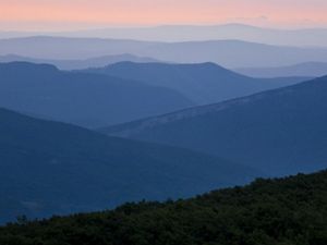 Mountain ridges are outlined in dark blue against the pink sky of a setting sun.