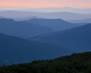 Mountain ridges are outlined in dark blue against the pink sky of a setting sun.