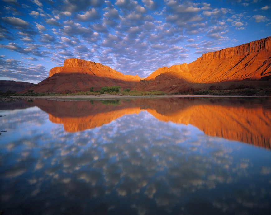 A red rock formation reflects in still waters.