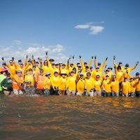 Dozens of TNC staff all wear yellow t-shirts and stand as a group knee-deep in water.