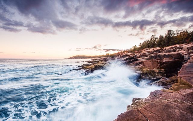 Waves crashing against the rocky coast of Acadia National at sunset in Maine.