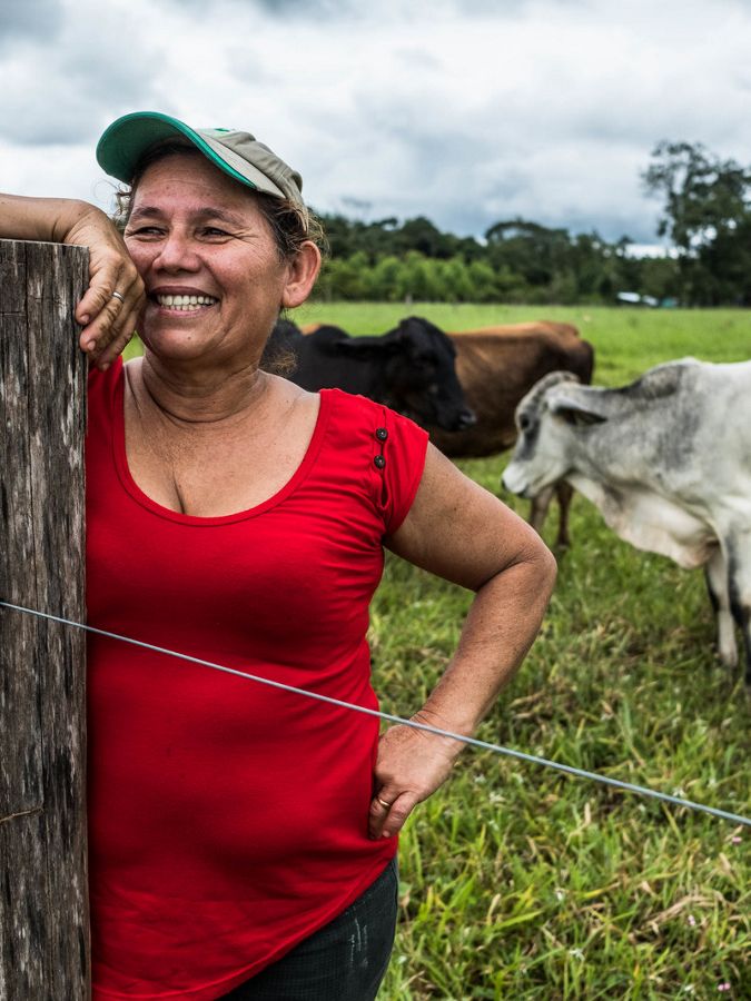 Female rancher in red shirt smiles against a fence post