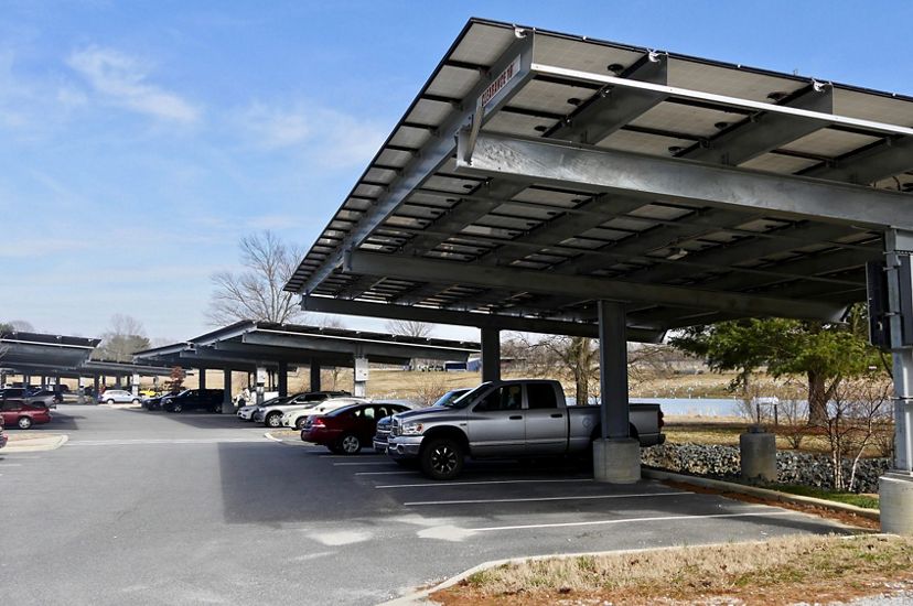 Cars at a commuter lot are parked underneath elevated solar panels that generate energy while shading the vehicles.