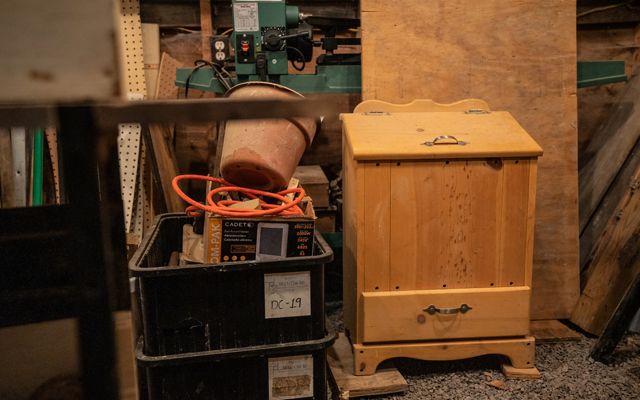 A wooden cabinet sitting on the floor of a wood shop with boxes beside it. 